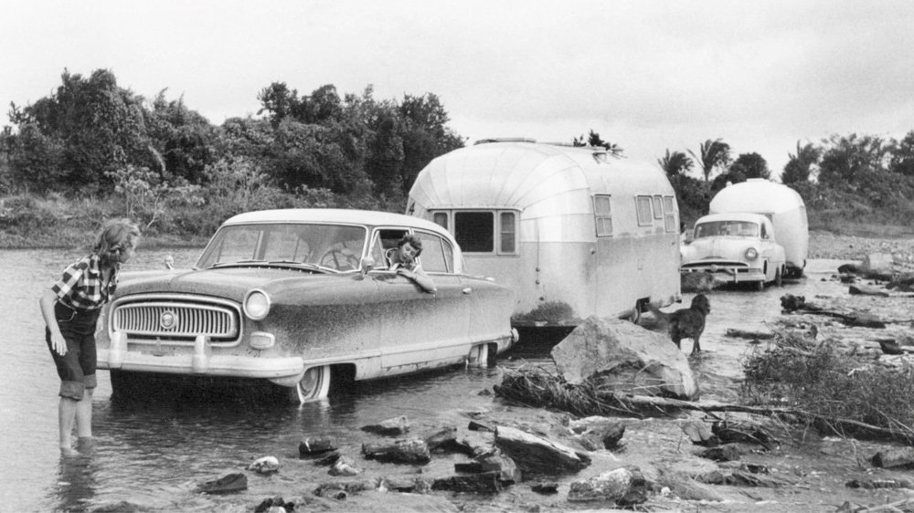 Travelers towing their airstream trailers navigate a muddy crossing.