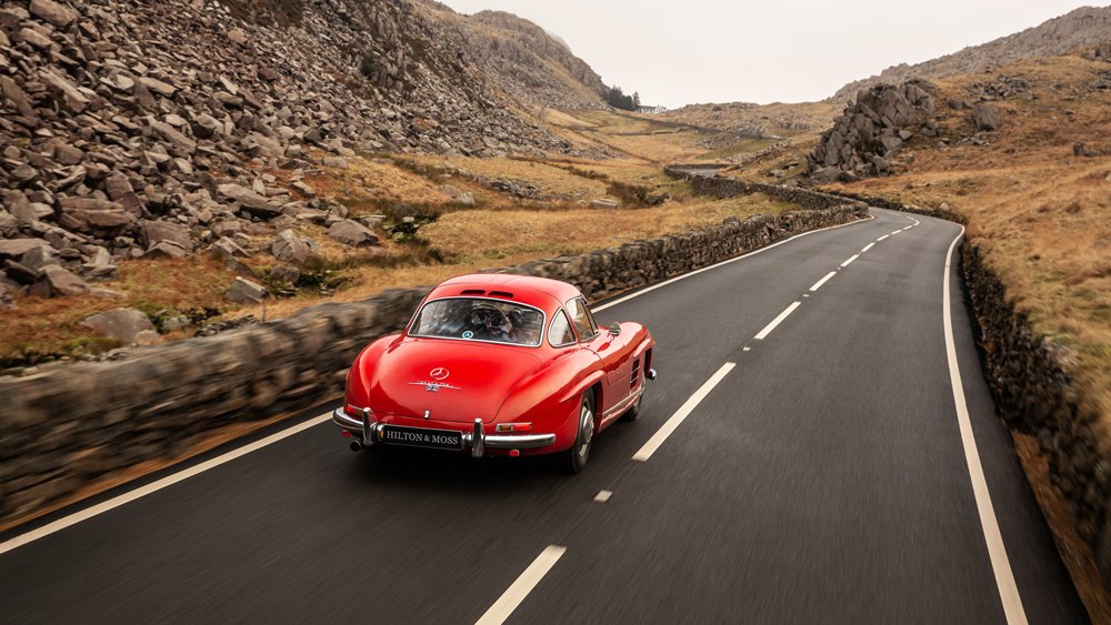 Driving a 1956 Mercedes-Benz 300 SL Gullwing on a country road in the United Kingdom.