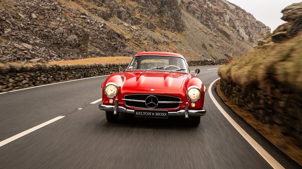 Driving a 1956 Mercedes-Benz 300 SL Gullwing on a country road in the United Kingdom.
