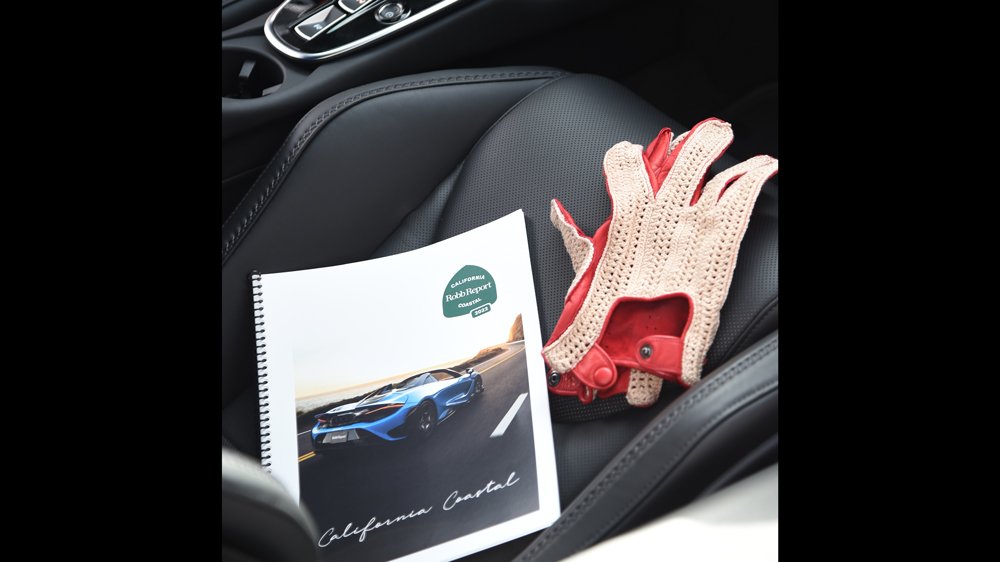 A road guide and driving gloves sit on the passenger seat of a car entered in the 2022 Robb Report California Coastal road rally.