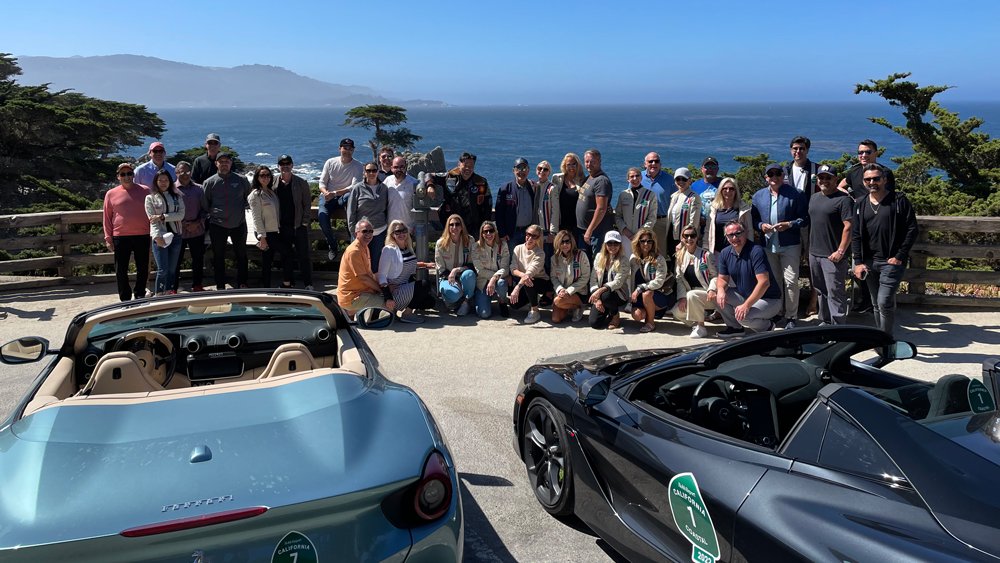Members of the 2022 Robb Report California Coastal road rally pose in front of the famous Lone Cypress along 17-Mile Drive in Pebble Beach.