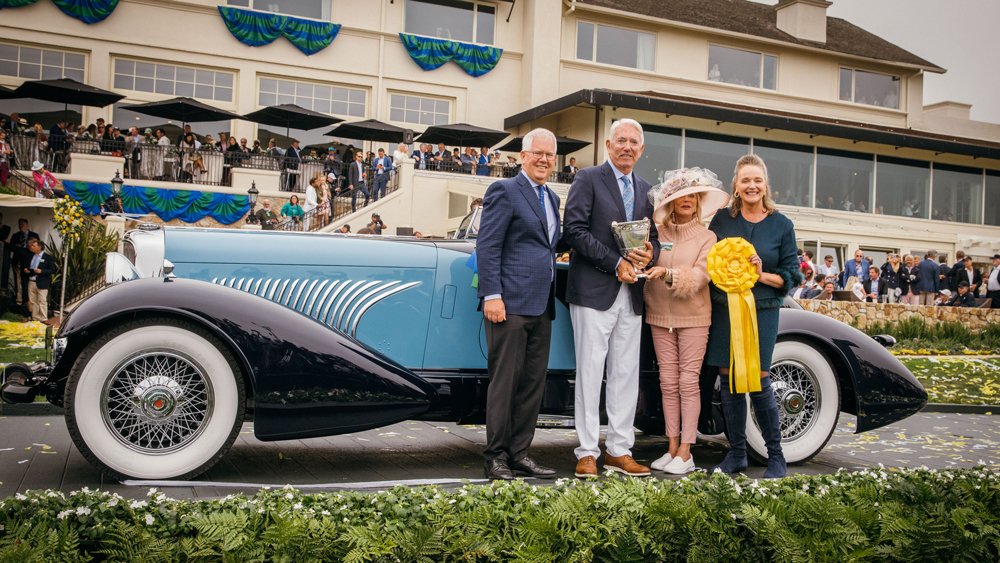 Sandra Button, chairman of the Pebble Beach Concours d'Elegance (right) and David Stivers, CEO of the Pebble Beach Company (left) award Lee and penny Anderson Best of Show for their 1932 Duesenberg J Figoni Sports Torpedo at the 2022 Pebble Beach Concours d'Elegance.
