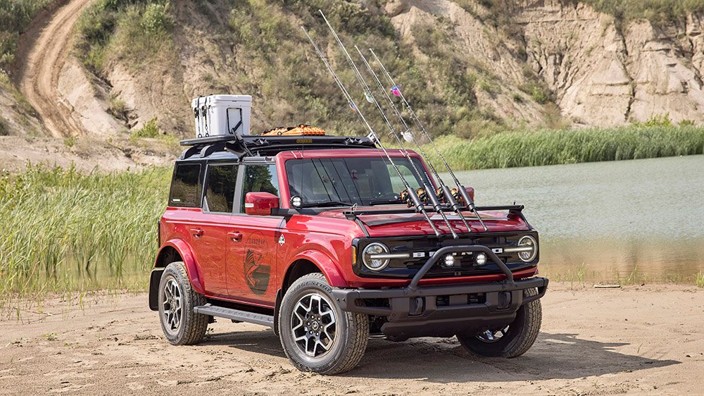 Bronco Four-Door Outer Banks Fishing Guide. Purpose-built to support a professional fishing guide along Cape Hatteras National Seashore, this lifestyle concept is based off the regionally inspired four-door Bronco Outer Banks™ series. On top is a Bestop® Sunrider® first-row soft top, factory-style concept roof rails and crossbars, and a Yakima® LockNLoad™ Platform roof rack. The SUV makes use of fender-mounted trail sights to fit a custom-made fishing pole and seat perch to wait for the perfect catch. A Ford Performance modular front bumper and safari bar help push through rugged terrain, while a slide-out tailgate* provides a great work surface when repairing fishing rods or stringing up new lures. All-weather floor mats and splash guards round out the package. (Preproduction image with optional features shown. Available beginning Spring 2021.) (*Available late 2021)