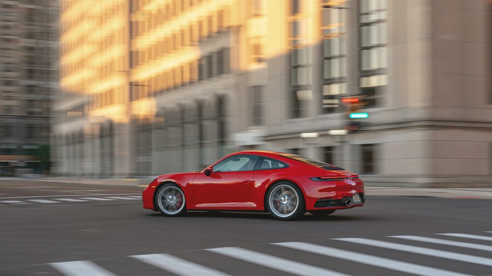 A Porsche 911 Carrera S, in Guards Red, is driven through a downtown intersection.