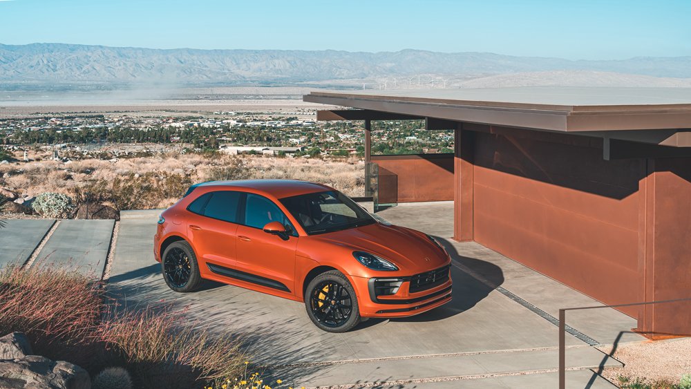 A Porsche Macan, in Papaya Metallic, parked in front of a residence.
