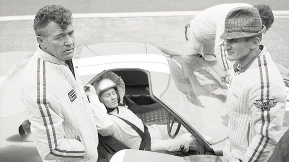 Carroll Shelby (left) and Ken Miles (standing on the right) at a racetrack.
