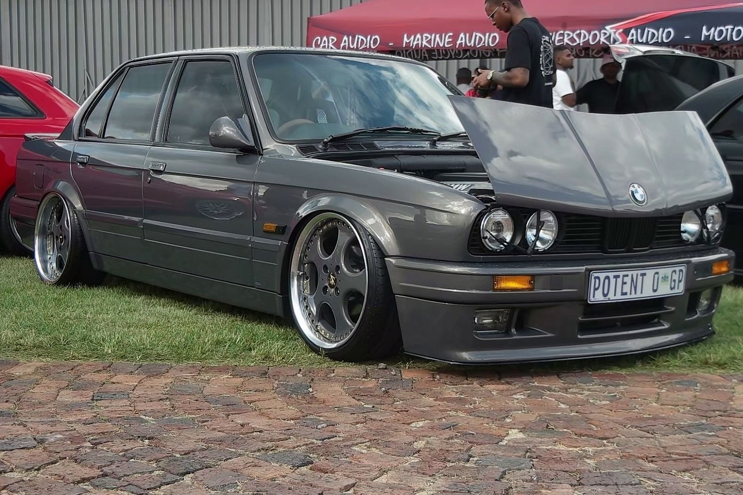 A modified BMW E30 parks at a car show.